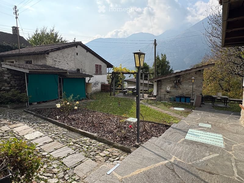 Stone pathway, flowers, trees, plants, garden lamp, tables, houses in the background, mountain view
