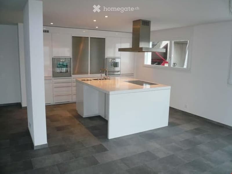Modern kitchen with white cabinets, stainless steel appliances, a central island, and a range hood. The floor is dark slate tiles, and there are windows above the sink.
