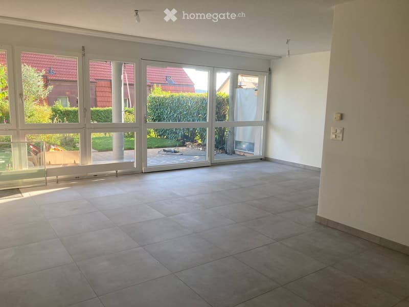 Empty room with tiled floor, large sliding glass doors leading to an outdoor area, and natural light from windows.