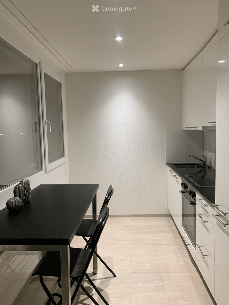 Modern kitchen with white cabinets, black countertop, sink, and a small dining area with a table and chair.