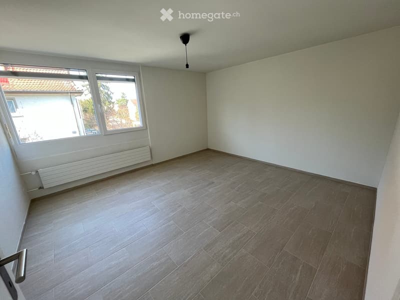 Empty room with tiled floor, white walls, large windows, radiator, and a ceiling light fixture.