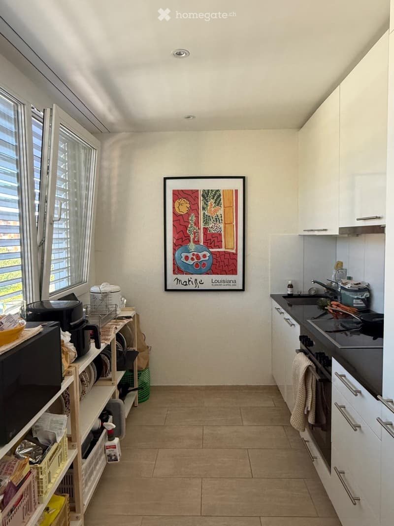 Modern kitchen with white cabinets, black countertops, and a large window. Includes a microwave, coffee maker, oven, sink, and a framed picture on the wall.