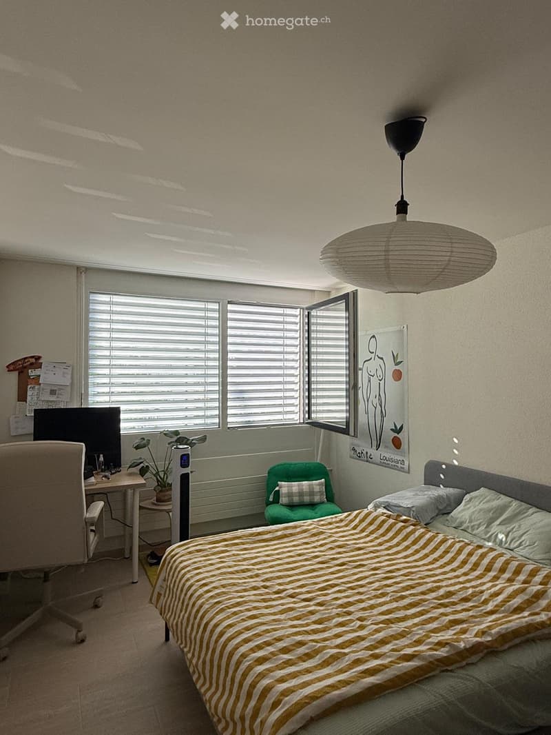 Cozy bedroom with a bed, desk, chair, green armchair, and a hanging lamp.