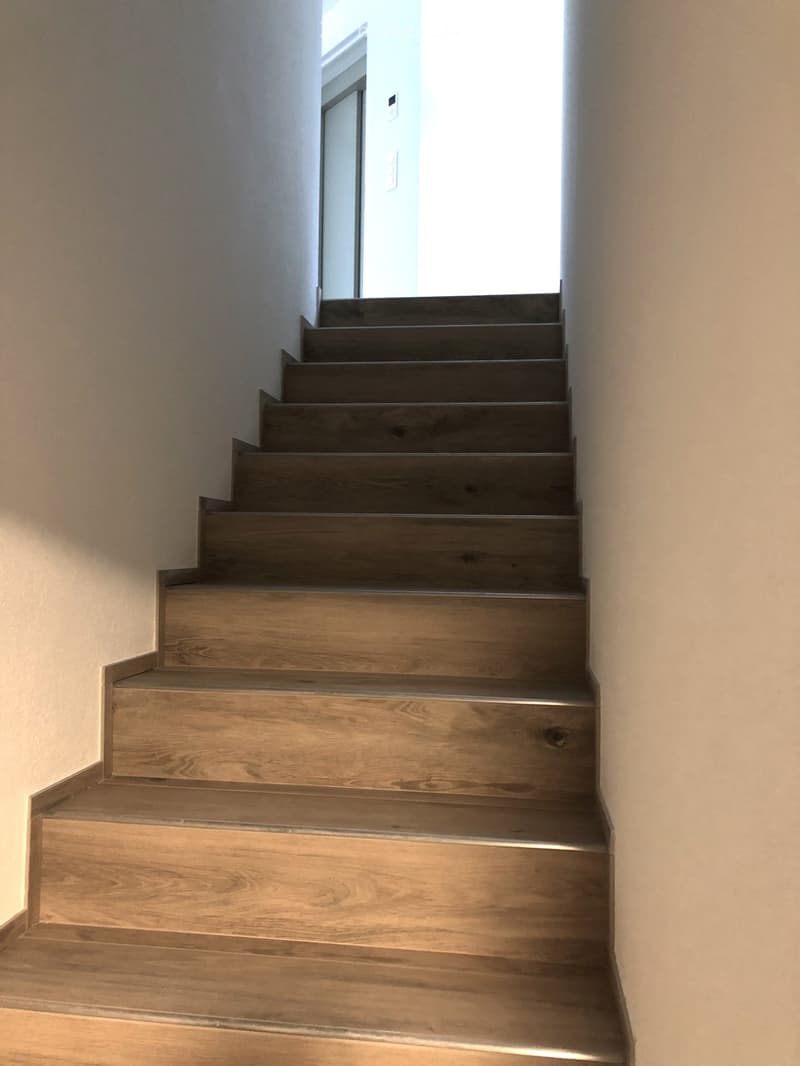 Wooden staircase with modern design, leading upwards, with natural light coming from the top.
