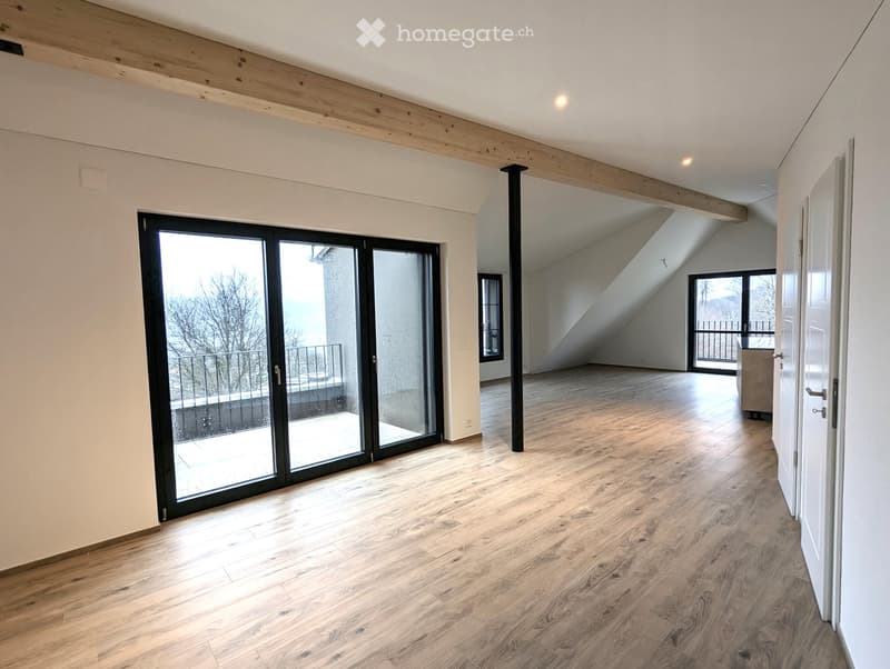Bright, unfurnished room with wooden flooring, white walls, and large sliding glass doors leading to a balcony. Exposed wooden beams on the ceiling and a visible attic space in the background.