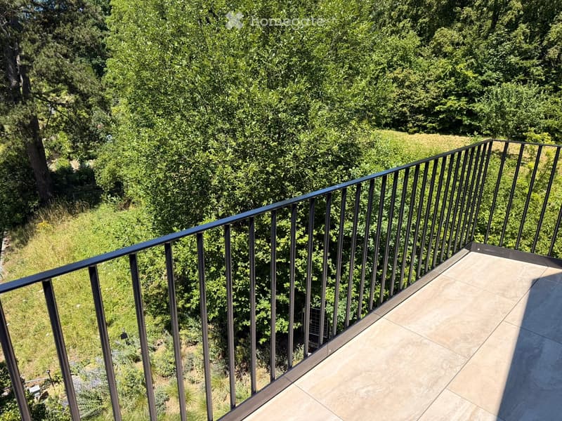 Balcony with modern metal railing and tiled floor, overlooking a lush green garden area.