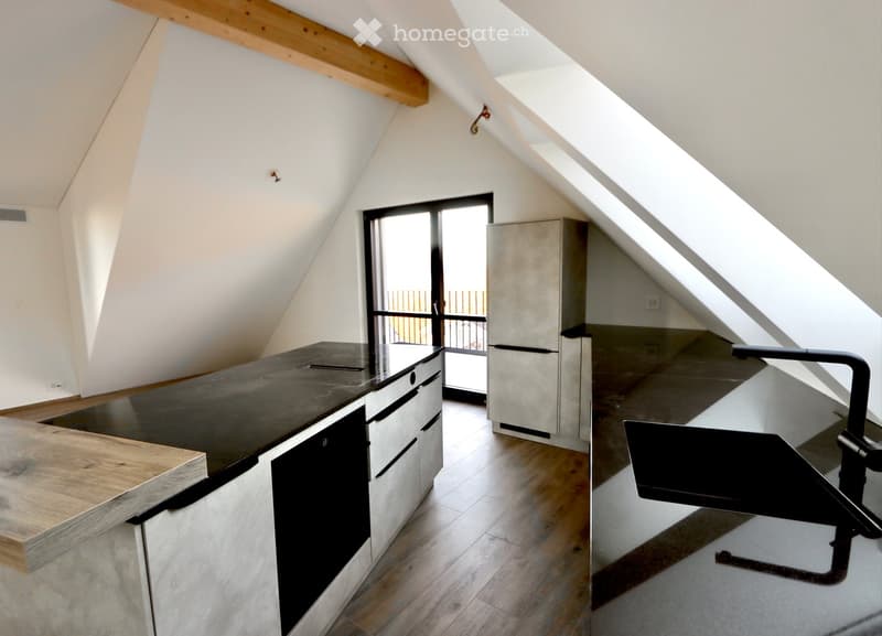 Modern kitchen with a central island, stainless steel appliances, and a balcony access through large windows.