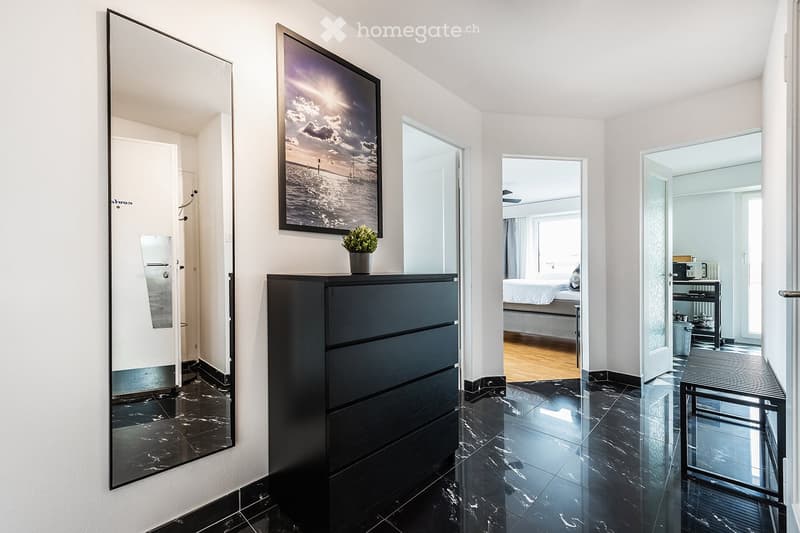 Modern hallway with black marble flooring, large mirrors, a black dresser with a small plant on top, and a framed picture on the wall. The hallway leads to a bedroom and a bathroom.