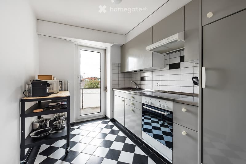 Modern kitchen with grey cabinets, black and white checkered floor, stainless steel appliances, and a small cart with kitchen utensils.