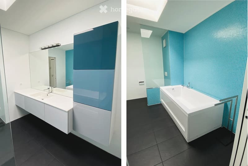Modern bathroom with a white sink, large mirror, and a bathtub. The walls feature blue tiles, and the floor is black tiled.