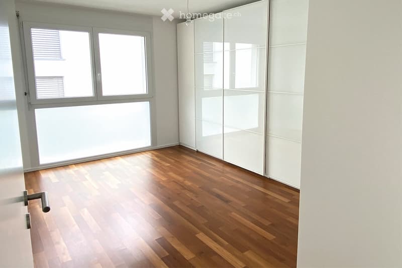 Empty room with wooden flooring, large windows, and white sliding closet doors.