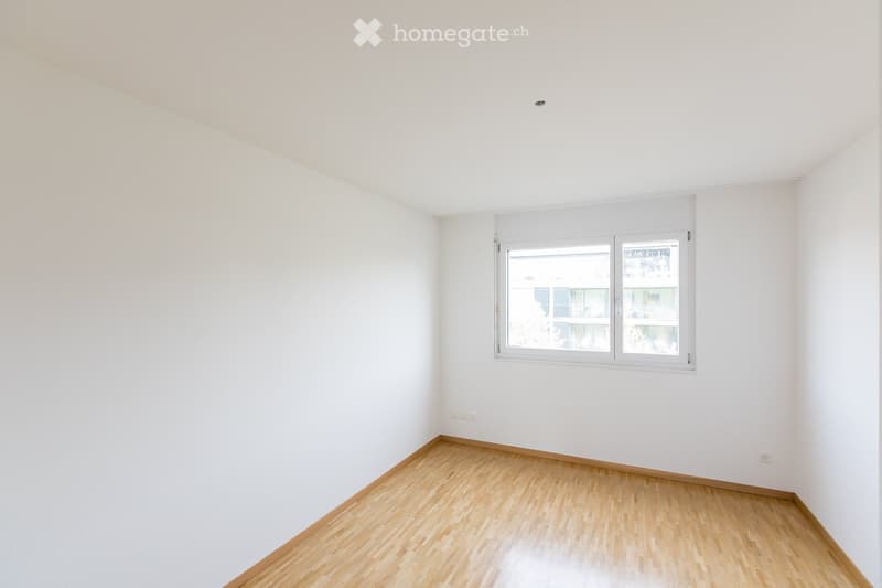 Empty room with white walls, wooden flooring, and a large window with white frame. No furniture or equipment present.