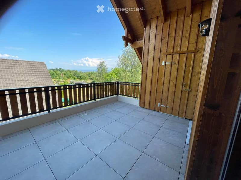 Balcony with tiled floor, wooden railings, and a view of a rural landscape with trees and a neighboring building.