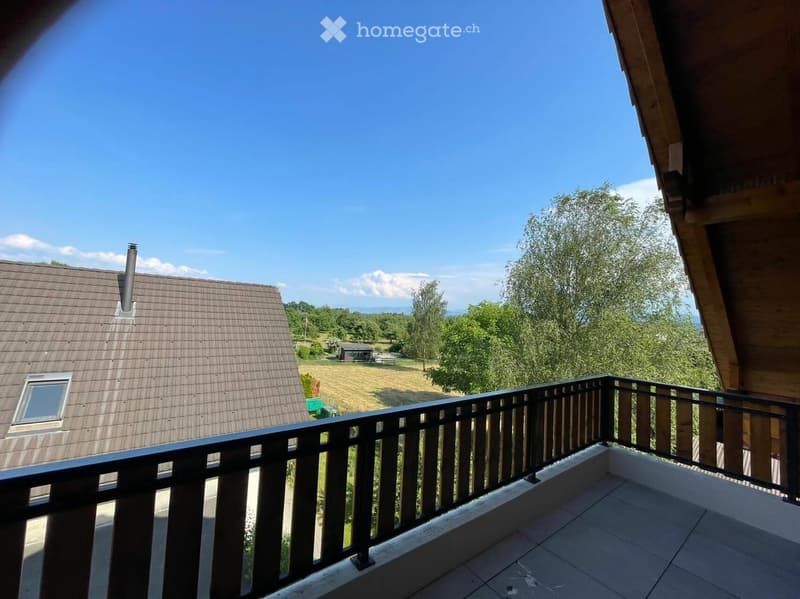 Balcony with wooden railing overlooking a rural landscape with fields, trees, and a neighboring house.