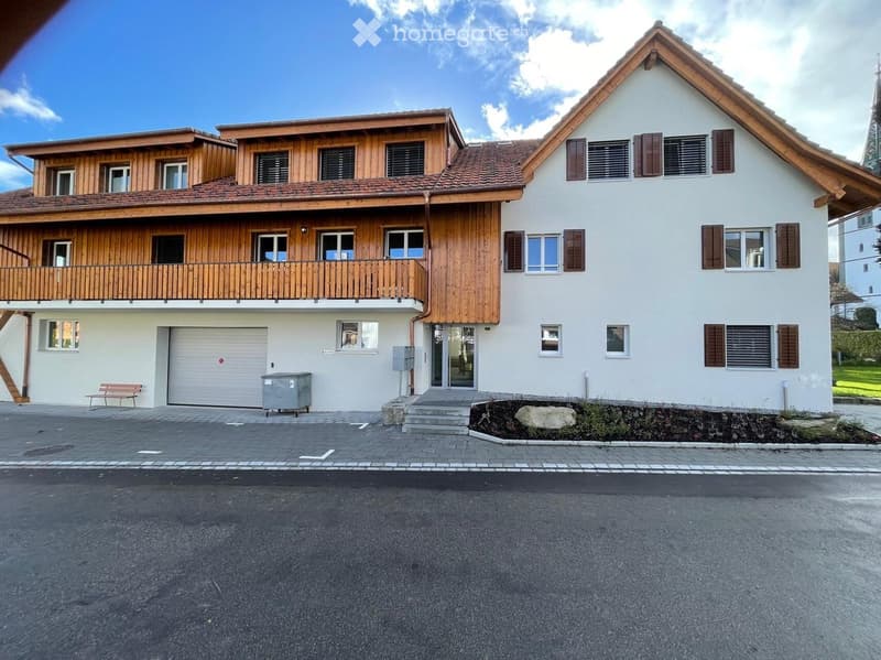 Two-story house with white walls, wooden balcony, garage, and steps leading to the entrance.