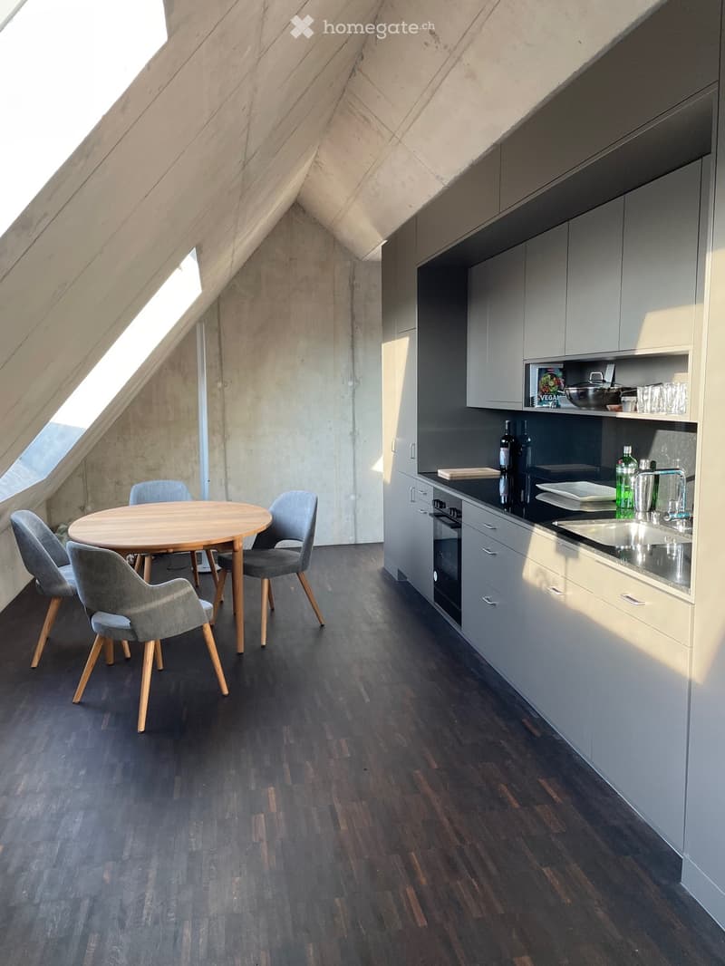 Modern kitchen with grey cabinets, dark wooden floor, round wooden dining table with four grey chairs, and various kitchen appliances and items on the counter.