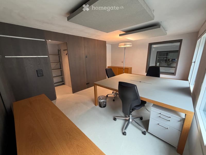 Modern office space with a large desk, ergonomic chairs, a floor lamp, a cabinet, and a mirror on the wall.