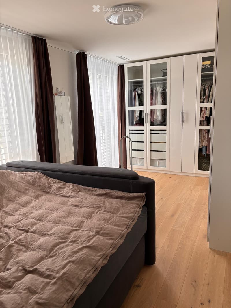 Modern bedroom with a large bed, white wardrobes, and large windows with curtains.