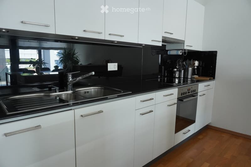 Modern kitchen with white cabinets, black countertops, stainless steel sink, and various kitchen utensils on the counter.