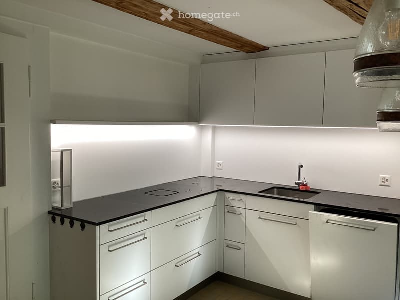 Modern kitchen with white cabinets, black countertop, stainless steel sink, and built-in lighting.
