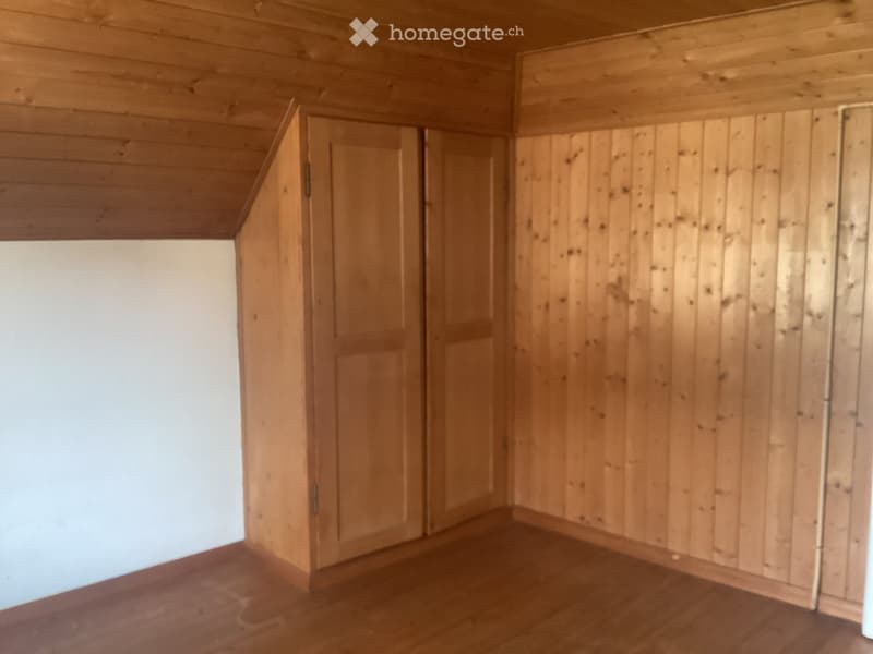 Empty room with wooden walls and floor, featuring a door and a slanted ceiling.