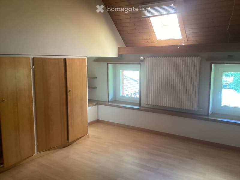 Empty attic room with wooden floors, slanted wooden ceiling, skylight window, and built-in window seat with radiator cover.