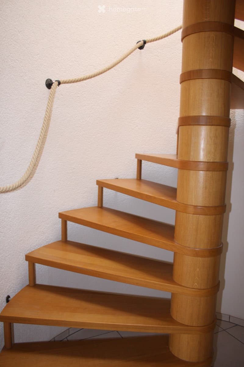 Wooden staircase with a central cylindrical wooden post and rope handrail, featuring multiple wooden steps and platforms.