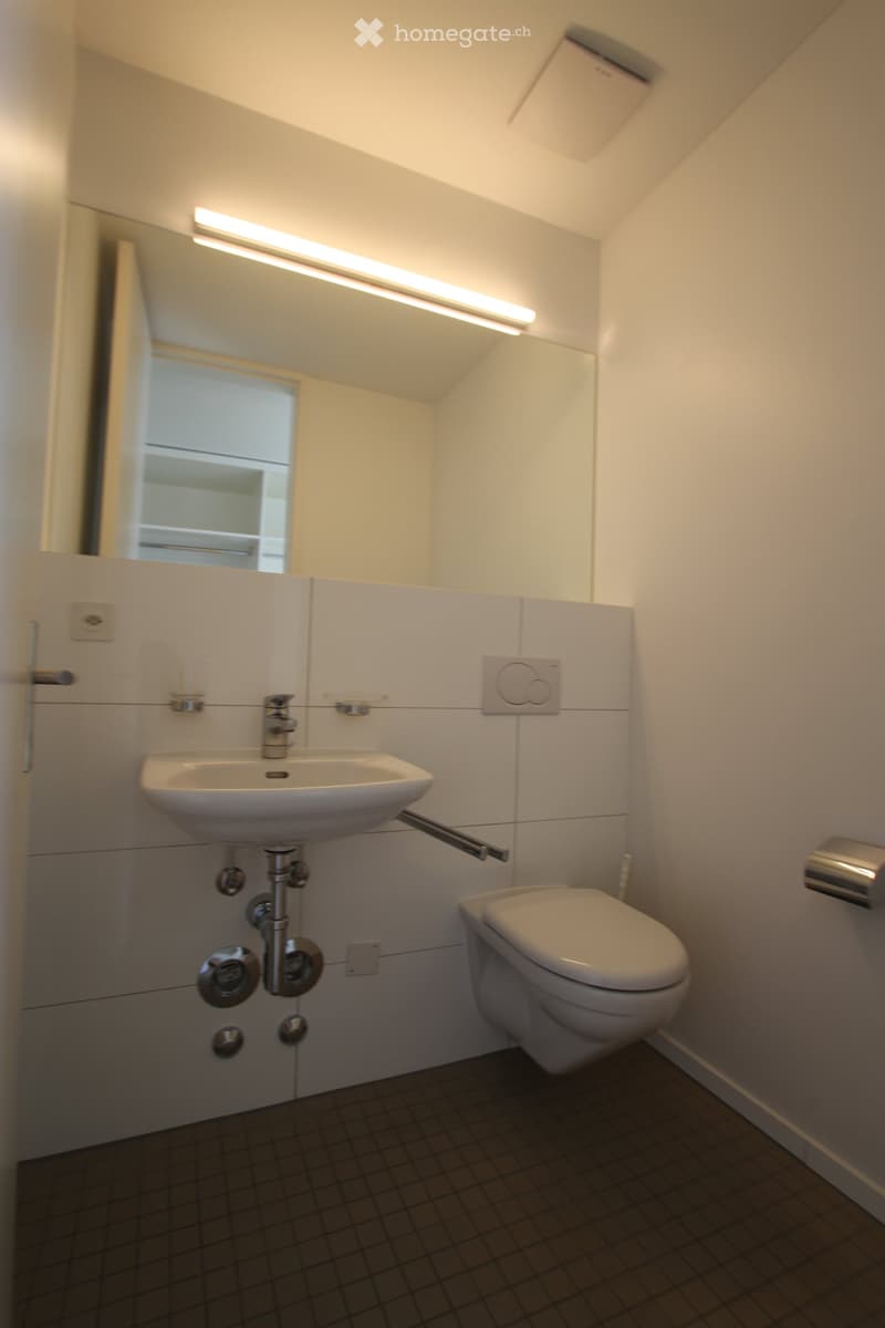 Modern bathroom with a white sink, chrome faucet, toilet, large mirror with built-in lighting, and tiled walls and floor.
