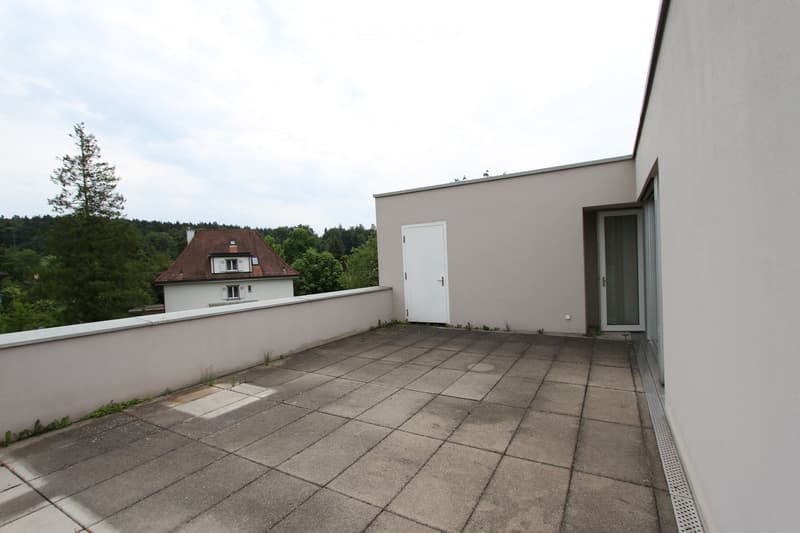 Balcony with tiled floor, low wall, access door, and view of a house and greenery.