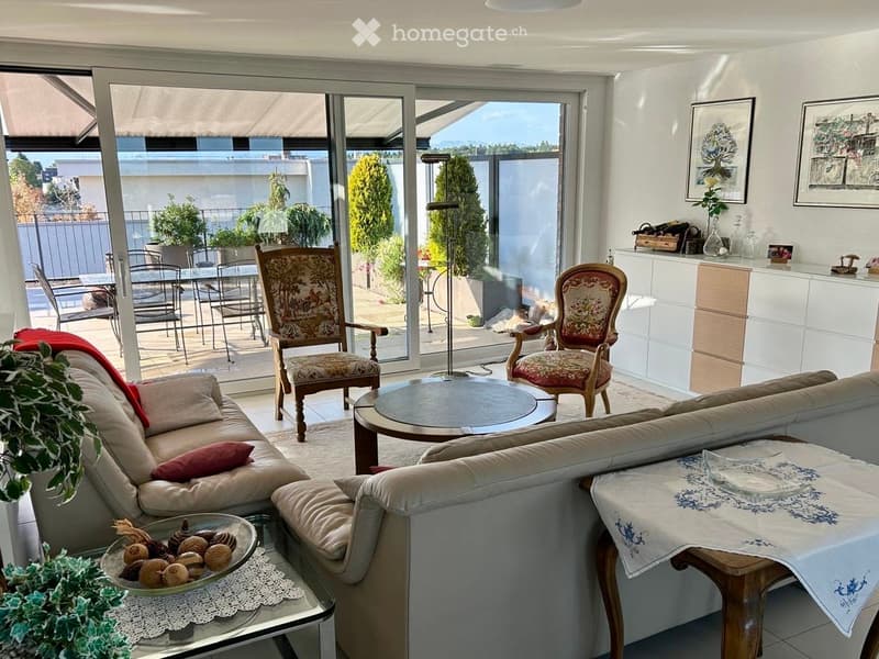 Bright living room with large sliding glass doors opening to a balcony, featuring a beige sectional sofa, coffee table, two armchairs, a round table, and a small side table with a decorative tablecloth.