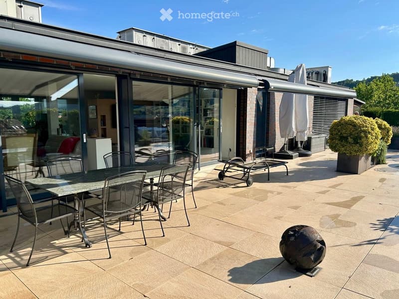 Roof terrace with tiled flooring, a dining table with chairs, sun loungers, and an umbrella. The terrace is connected to an indoor living space through large glass doors.
