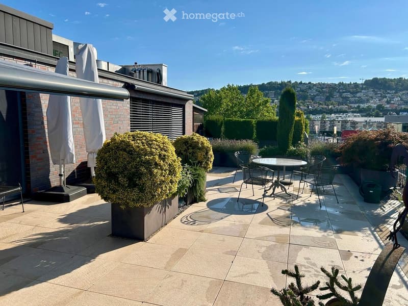 Roof terrace with tiled floor, round table, chairs, potted plants, and a scenic city view.