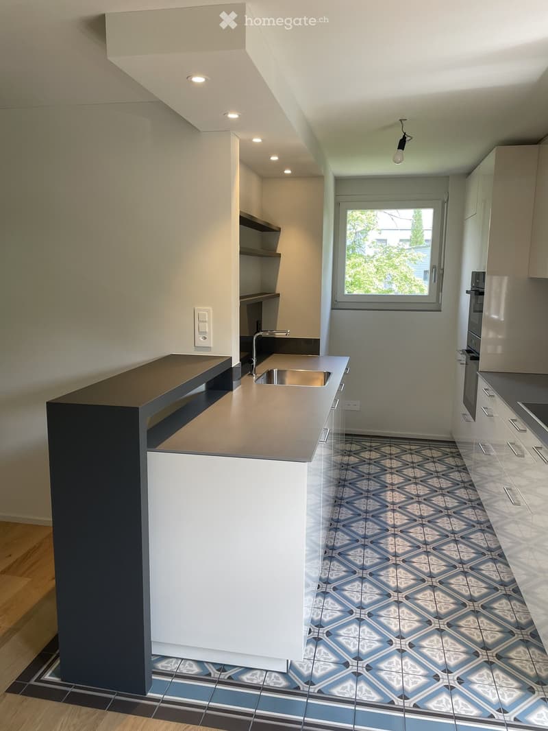 Modern kitchen with white cabinets, a dark countertop, and a stainless steel sink. The floor features blue and white patterned tiles.