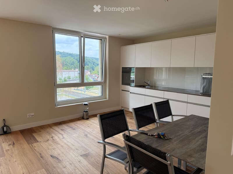 Modern kitchen with white cabinets, a large window overlooking a scenic view, a wooden dining table with four black chairs, and a blender on the floor.