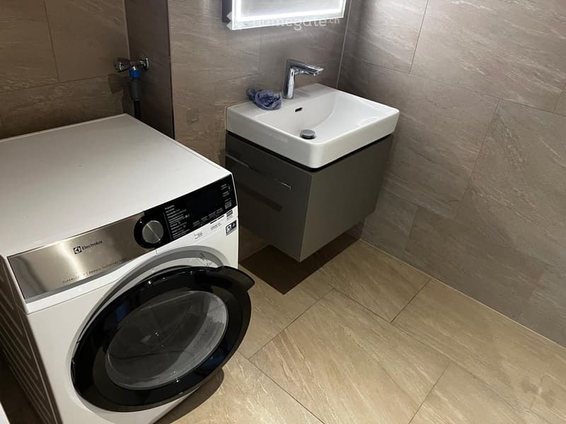 Modern bathroom with a white sink, chrome faucet, and a white washing machine with an open door.