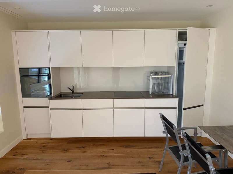 Modern kitchen with white cabinets, stainless steel appliances, and a small dining area with chairs and a table.