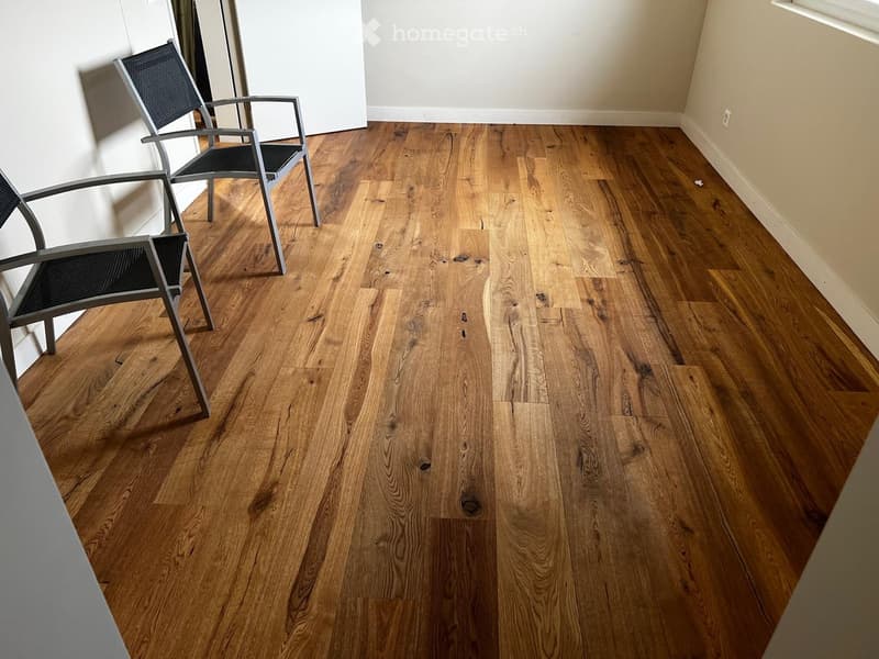 Empty room with polished hardwood flooring and two modern metal chairs against the wall.