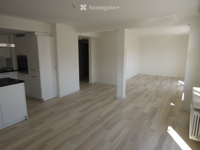 Open-plan living and kitchen area with light wooden flooring, white cabinets, and modern appliances.