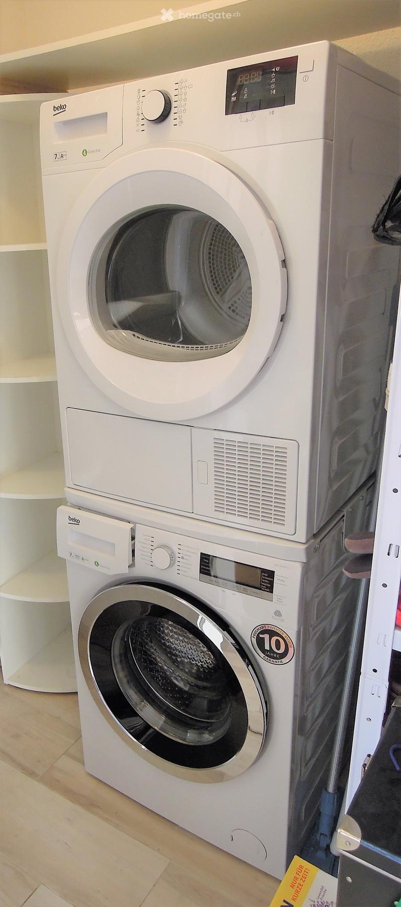 White washing machine and dryer stacked vertically in a bathroom with wooden flooring.