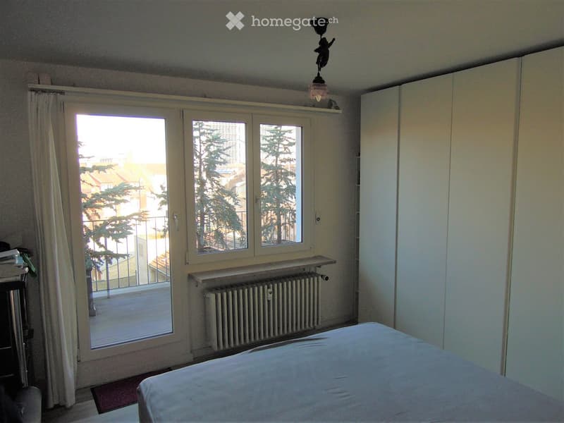 Bright bedroom with a large window and balcony access, featuring a bed, wardrobe, and radiator.