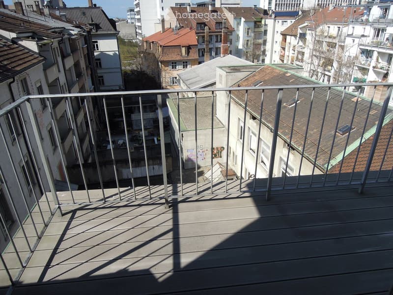 Balcony with wooden decking and metal railing, overlooking a cityscape with multiple buildings and rooftops.