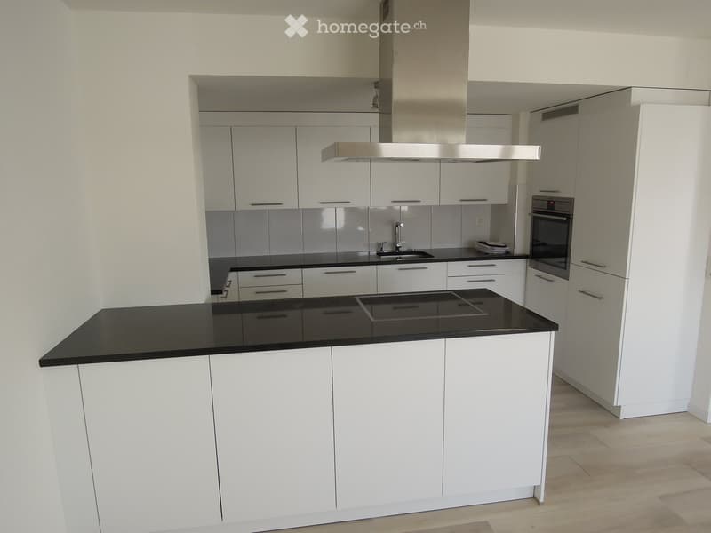 Modern kitchen with white cabinets, black countertop, stainless steel appliances, and a central island.
