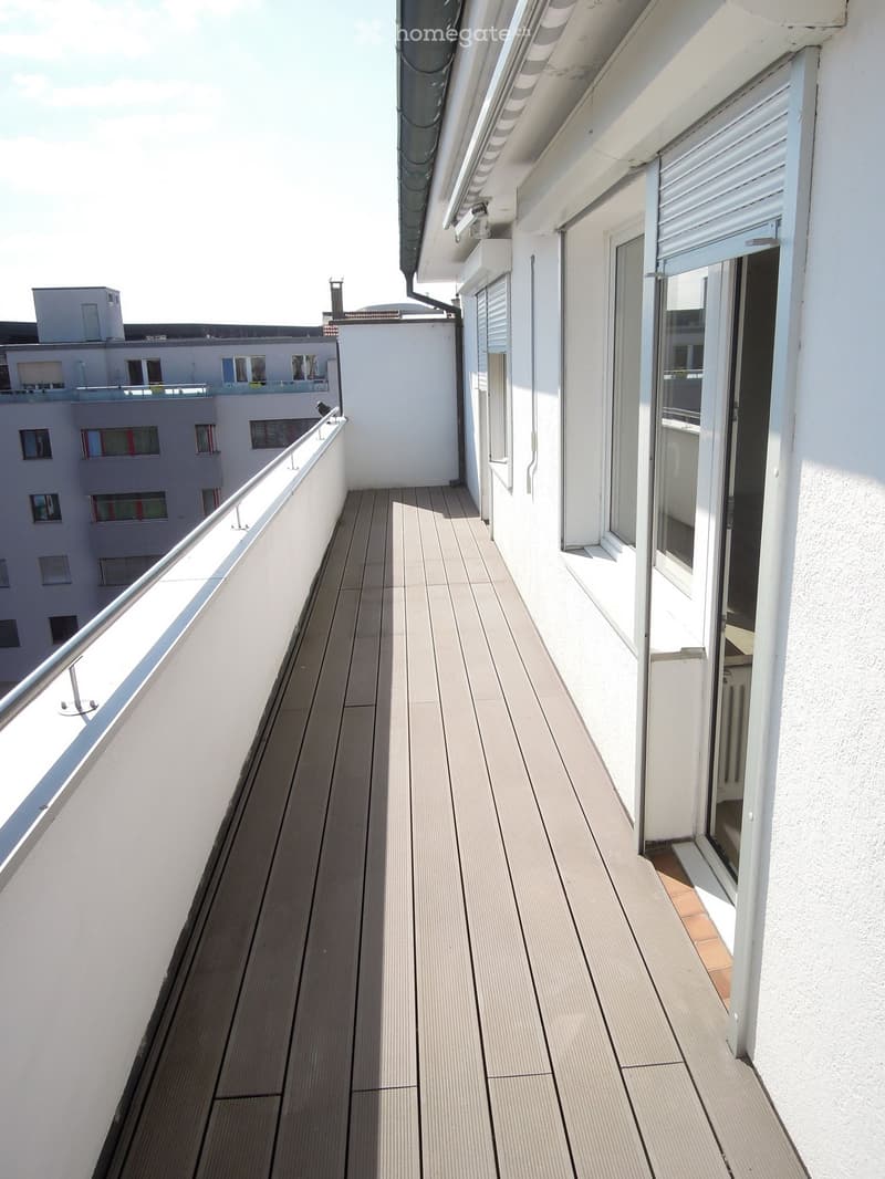 Balcony with wooden decking, white railing, and sliding glass door leading to the interior.