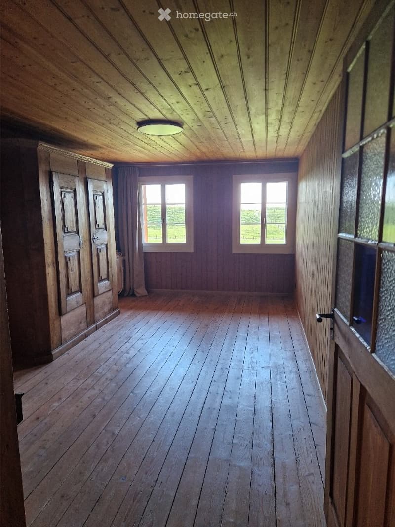 Empty room with wooden walls, ceiling, and floor, two windows, and a single light fixture.