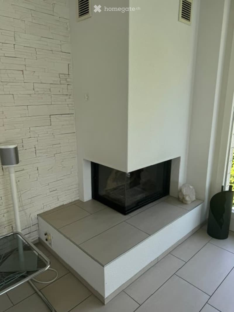 Modern living room with a built-in fireplace, white brick accent wall, and large windows. Includes a sleek glass coffee table and a contemporary floor lamp.