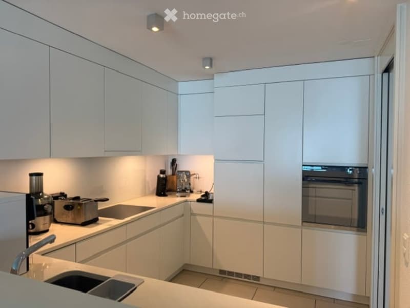 Modern, minimalist kitchen with white cabinetry, stainless steel appliances, and a clean, organized workspace.