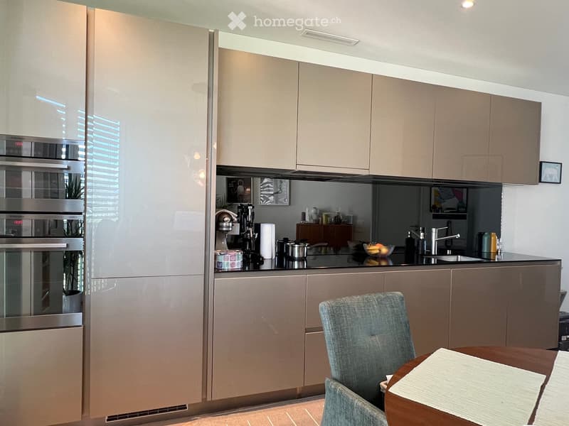 Modern kitchen with light wood cabinets, stainless steel appliances, and a black countertop. Includes a dining area with a table and chairs.