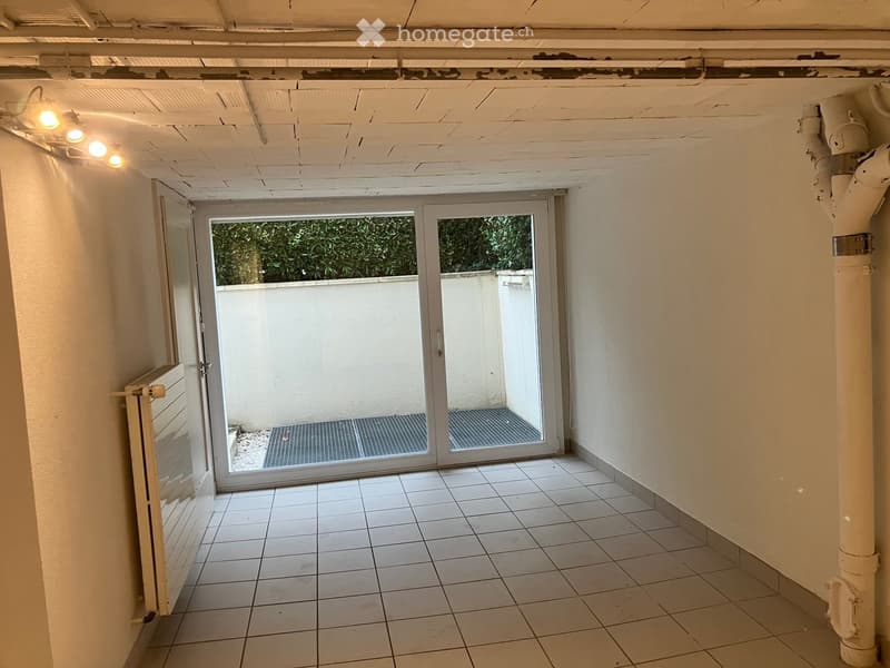 Empty room with white tiled floor, white walls, and a sliding glass door leading to an outdoor area.