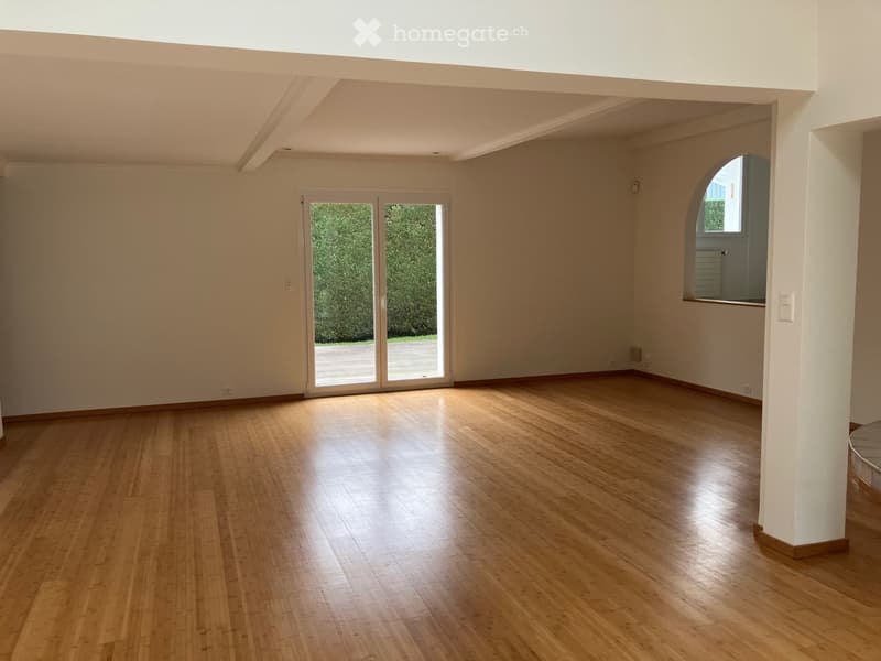 Empty room with wooden flooring, white walls, large sliding glass door leading outside, and an arched window on the right side.