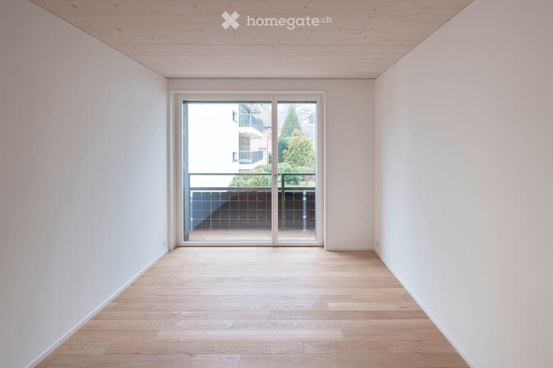 Empty room with light wooden flooring, white walls, and a large sliding glass door leading to a balcony.